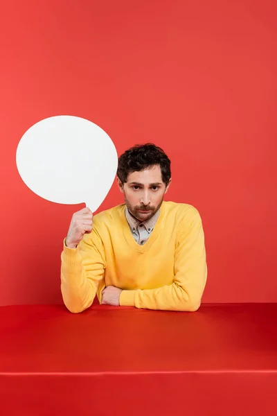 Bearded man in yellow long sleeve jumper holding blank speech bubble on red coral background — Stock Photo