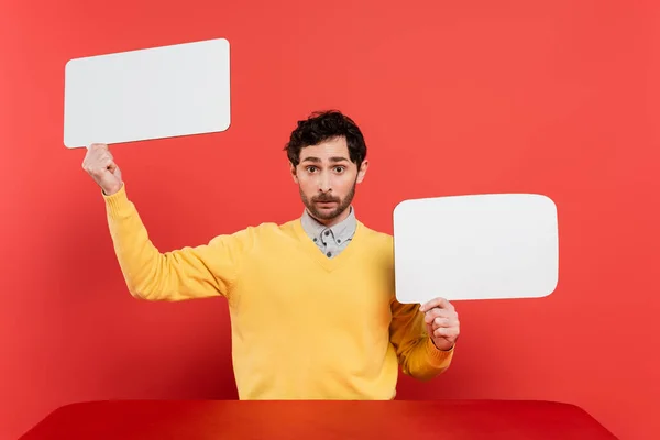 Bearded man in yellow long sleeve jumper holding blank speech bubbles on red coral background — Stock Photo