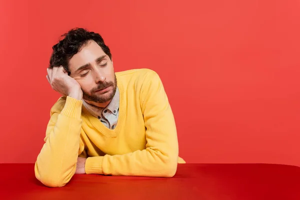 Uomo stanco in giallo maglione a maniche lunghe che dorme alla scrivania isolato su sfondo corallo — Foto stock