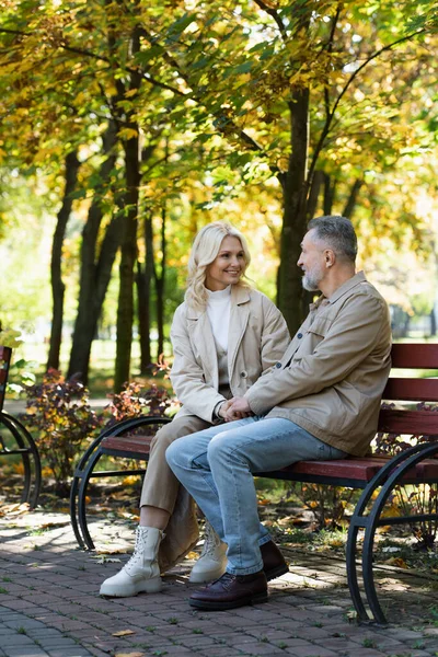 Cheerful mature couple talking on bench in autumn park — Stock Photo