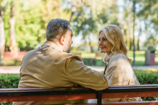 Зрелая пара разговаривает, сидя на скамейке в весеннем парке — стоковое фото