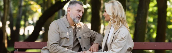 Mature man talking to blonde wife while spending time together in park, banner — Stock Photo