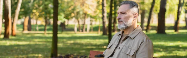 Mature homme regardant loin tout en passant du temps dans le parc flou, bannière — Photo de stock