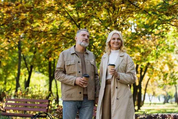 Позитивная зрелая пара держит бумажные стаканчики во время прогулки в парке — стоковое фото