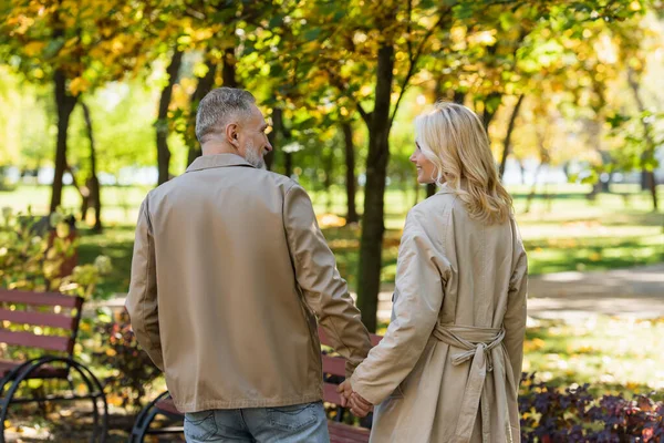 Vista lateral do casal de meia idade despreocupado de mãos dadas enquanto caminha no parque — Fotografia de Stock