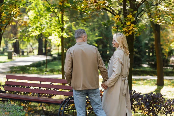 Positive mature couple holding hands while walking in park at daytime — Stock Photo