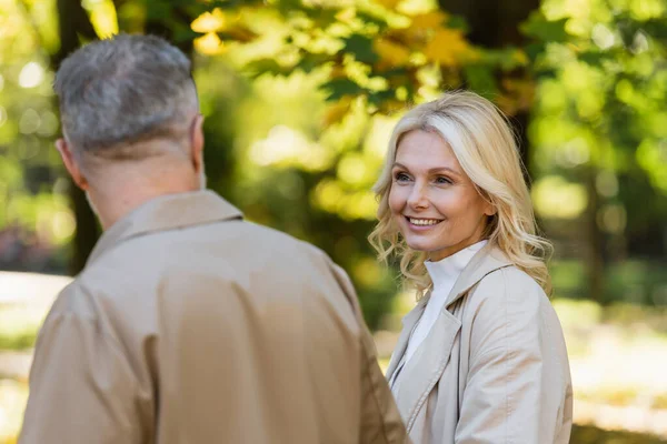 Mulher loira positiva olhando para o marido desfocado no parque — Fotografia de Stock