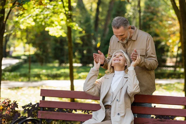 Веселая женщина смотрит на мужа средних лет, сидя на скамейке в парке — стоковое фото