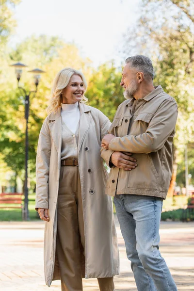 Sonriendo pareja madura hablando mientras camina en el parque de primavera - foto de stock