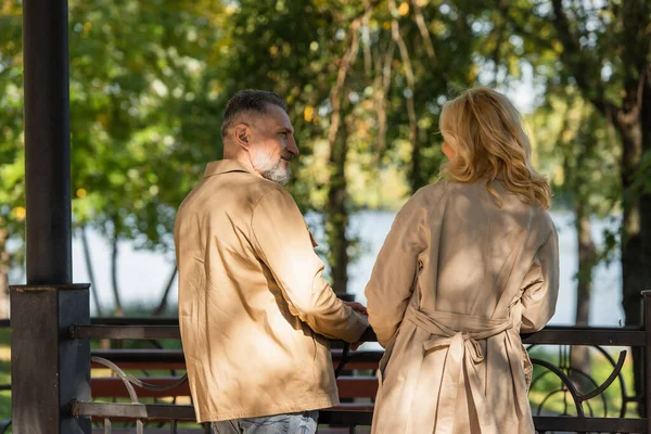 Smiling mature man talking to wife near bridge in spring park — Stock Photo