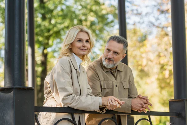 Mature man looking at smiling blonde wife near bridge in park — Stock Photo
