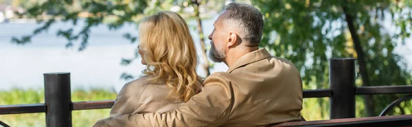 Зрелый мужчина обнимает жену-блондинку в весеннем парке, баннер — стоковое фото