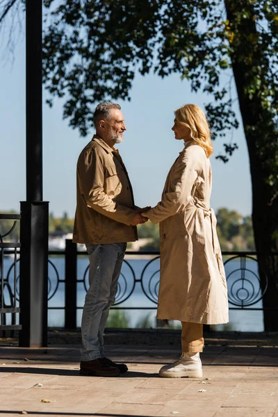 Seitenansicht eines lächelnden Paares mittleren Alters, das sich im Park an den Händen hält — Stockfoto