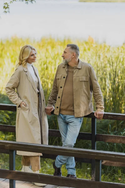 Пара середнього віку розмовляє, стоячи на мосту в весняному парку — стокове фото