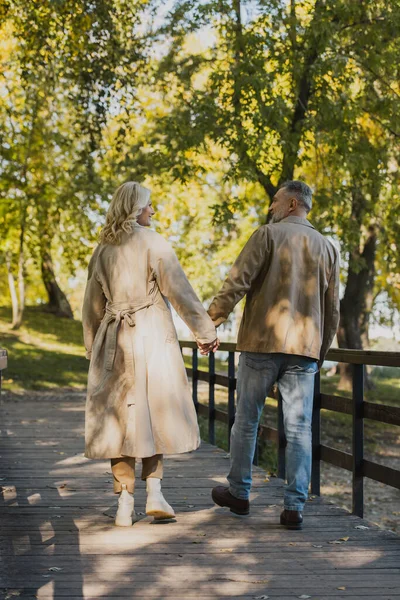 Vista lateral de pareja madura despreocupada conversando y caminando en el parque - foto de stock
