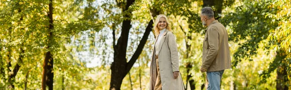 Счастливая женщина средних лет в повседневной одежде выходя с мужем в зеленом парке весной, баннер — стоковое фото