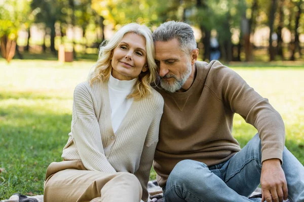Porträt eines charmanten Paares mittleren Alters, das im Frühling zusammen im grünen Park sitzt — Stockfoto