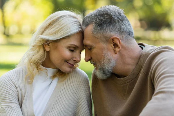 Happy middle aged couple sitting face to face with closed eyes during springtime — Stock Photo
