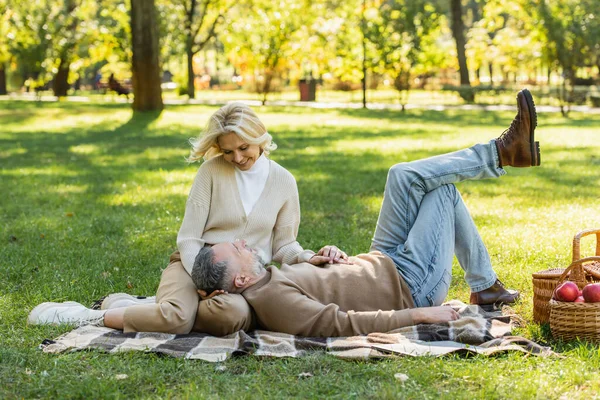 Bearded middle aged man lying on laps of happy wife during picnic in park — Stock Photo