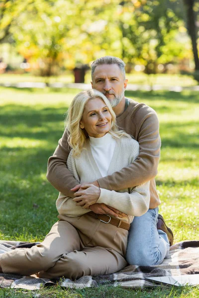 Middle aged man with grey beard hugging charming blonde wife in green park — Stock Photo