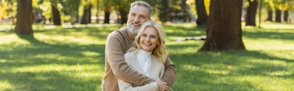 Super alegre homem de meia idade com barba cinza abraçando encantadora esposa loira no parque, banner — Fotografia de Stock
