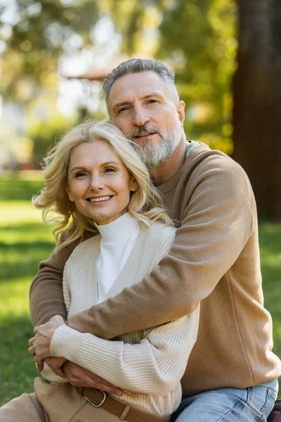 Alegre homem de meia idade com barba cinza abraçando feliz esposa loira no parque — Fotografia de Stock