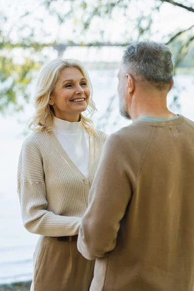 Счастливая женщина средних лет, глядя на бородатого мужа, держась за руки возле озера — стоковое фото