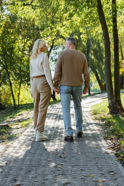 Повна довжина стильної пари середнього віку тримає руки під час прогулянки разом у зеленому парку — стокове фото