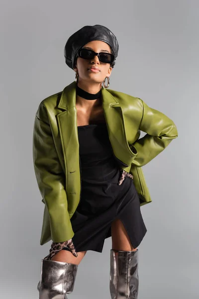 Modelo americano africano elegante em óculos de sol e casaco de couro posando isolado em cinza — Fotografia de Stock