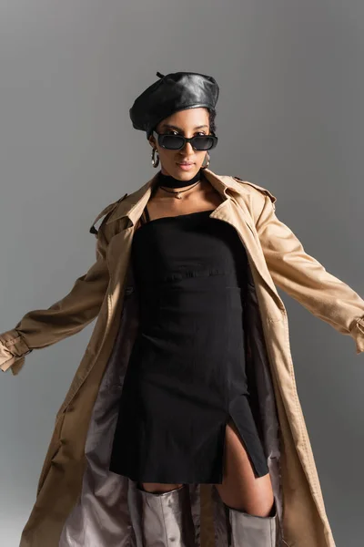 Modelo afroamericano de moda posando en gabardina y gafas de sol aisladas en gris - foto de stock