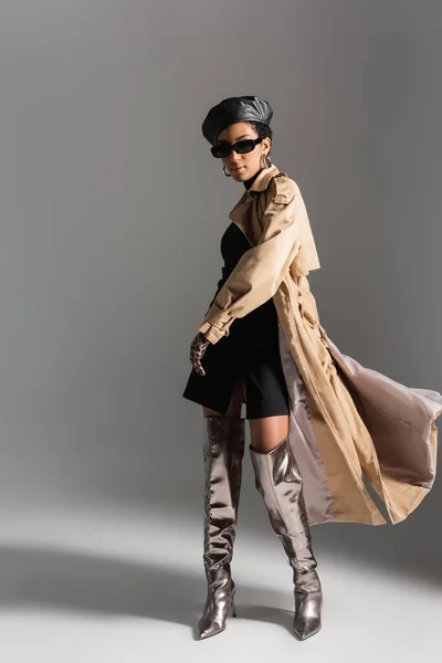 Volle Länge der modischen afrikanisch-amerikanischen Frau in Sonnenbrille und Trenchcoat auf grauem Hintergrund — Stockfoto