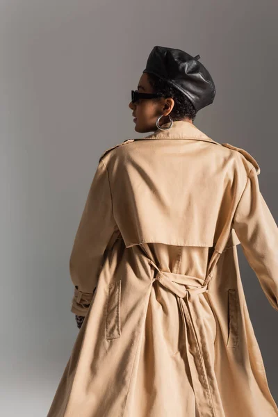 Vue latérale de la femme afro-américaine branchée en béret et trench coat isolé sur gris — Photo de stock