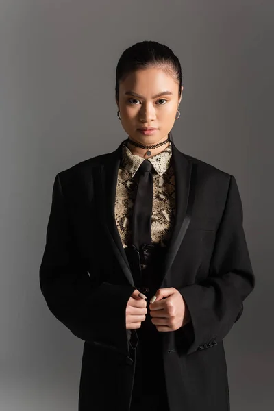 Elegante modelo asiático en chaqueta mirando cámara aislada en gris - foto de stock