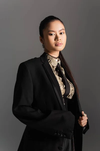 Portrait of asian model in black jacket looking at camera isolated on grey — Stock Photo
