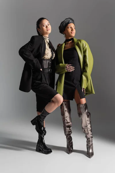 Longitud completa de modelos multiétnicos de moda en chaqueta y abrigo posando sobre fondo gris - foto de stock