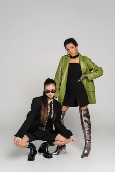 Junge multiethnische Freundinnen in stylischer Kleidung posieren auf grauem Hintergrund — Stockfoto