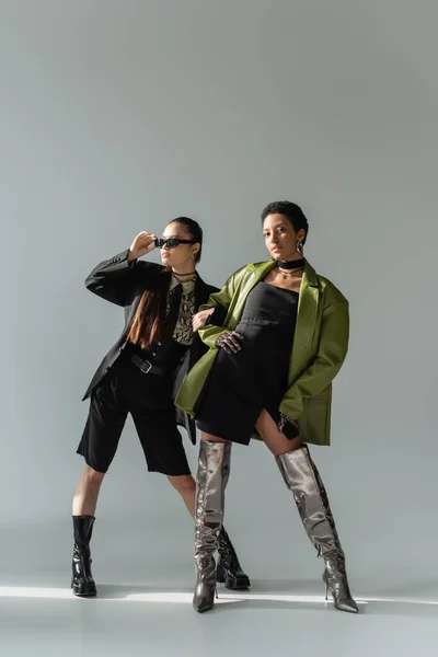 Lunghezza completa di fidanzate multietniche alla moda in piedi su sfondo grigio con luce solare — Foto stock