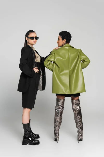 Full length of trendy asian model posing with african american friend on grey background — Stock Photo