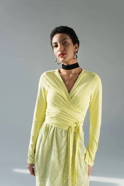 Mujer afroamericana de moda en traje amarillo mirando a la cámara sobre fondo gris - foto de stock