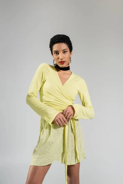 Pretty young african american model in yellow clothes standing isolated on grey — Stock Photo