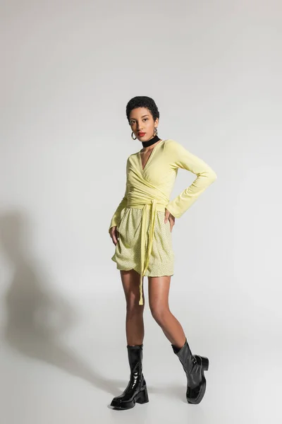 Comprimento total do elegante modelo afro-americano em roupas de primavera e botas em fundo cinza — Fotografia de Stock