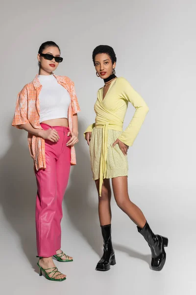 Межрасовые модели в красочной весенней одежде позируют на сером фоне — стоковое фото