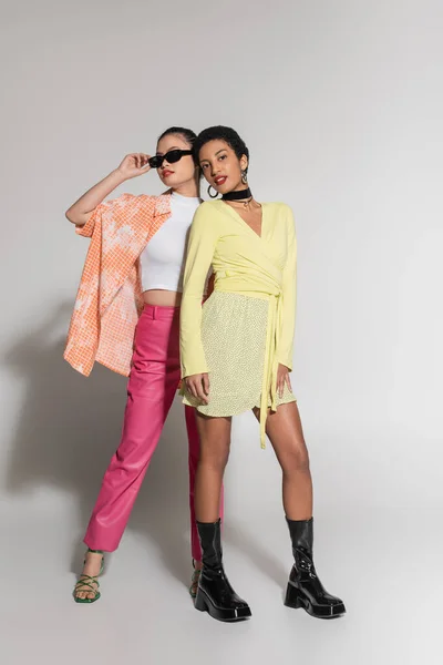 Comprimento total de modelos inter-raciais na moda em roupas coloridas em pé sobre fundo cinza — Fotografia de Stock