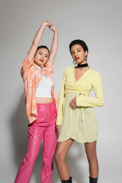Modelos multiétnicos elegantes em roupa brilhante posando em fundo cinza — Fotografia de Stock