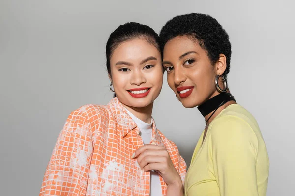 Trendy multiethnic women with makeup smiling at camera on grey background — Stock Photo