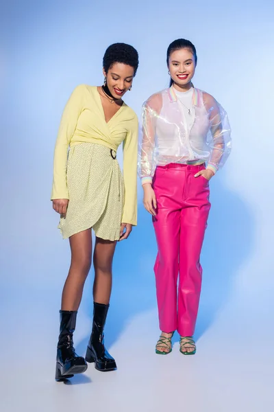 Lunghezza completa di modelli multietnici alla moda in abiti primaverili sorridenti su sfondo blu — Foto stock