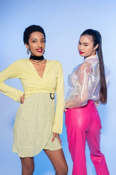 Unbekümmerte multiethnische Freundinnen im Frühlings-Outfit posieren auf blauem Hintergrund — Stockfoto