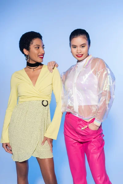 Carefree asian woman with red lips posing with african american friend on blue background — Stock Photo