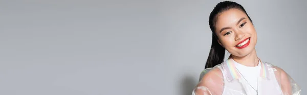 Positivo modello asiatico con labbra rosse in piedi su sfondo grigio, banner — Foto stock