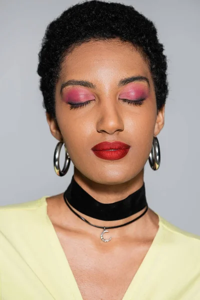 Porträt einer afrikanisch-amerikanischen Frau mit buntem Make-up, die die Augen isoliert auf grau schließt — Stockfoto